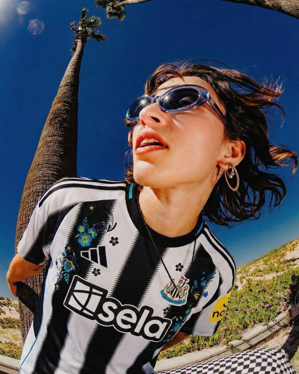 Model in a black and white striped club jersey seen from below, palm tree and blue sky behind